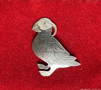 Front view of sterling silver puffin brooch on red background