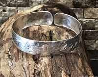 Front view of sterling silver child’s cuff bracelet showing floral engraving and open end