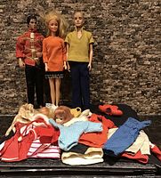 Overall view of three dolls standing with pile of clothing and accessories