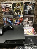 Front view of PlayStation 3 Slim console, controller, and seven PS3 game cases