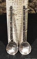 Front view of both sterling totem pole spoons standing