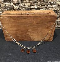 Necklace displayed on wooden block showing front drop section with three amber teardrop crystals