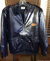 Front view of navy blue CAST puffy jacket on hanger showing zipper, pockets, logo patch