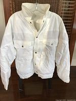 Front of white puffer jacket on hanger showing pockets and closure