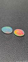 Both opal cabochons on black textured background showing colour play
