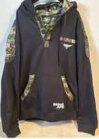 Front view of Rebel Ape hoodie on hanger showing camo accents and patches