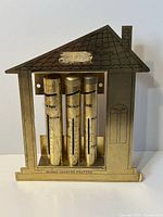 Front view of metal house-shaped coin counter bank showing three tubes and inscriptions