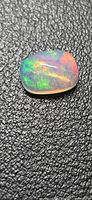 Cushion cabochon opal on black textured background showing green, orange play-of-color