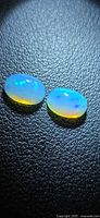 Two oval crystal opals on black textured surface showing play-of-color