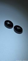 pair of black oval cabochon gemstones on neutral background