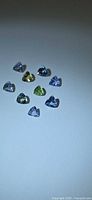 Nine small trillion-cut Tanzanite stones in various colors on a white background