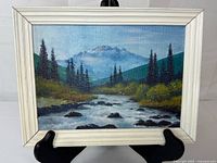 Front view of framed mountain landscape painting on easel