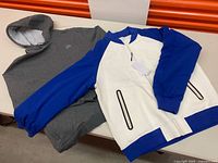 Grey Lacoste hoodie and white/blue Lacoste jacket laid out on table