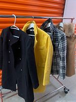 Four outerwear pieces on rack: black coat, yellow coat, houndstooth coat, tan cape