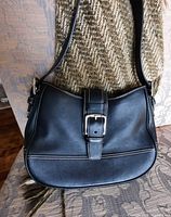 Front of black leather Coach purse hanging, shows overall style and strap