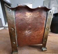 Front view showing hammered copper panel, brass corner straps, scalloped rim, brass feet