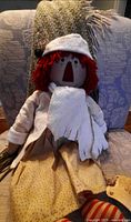 Full view of Raggedy Ann doll seated showing winter outfit and tag