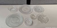 All seven clear pressed glass plates and bowls displayed on table