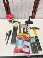 All items laid out including hammer, scraper, protractor, steel bar, chisel, screwdrivers, packaged consumables