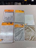 Six sealed Cricut Cuttlebug accessories laid out