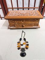 Ornate carved wooden jewelry box and bead necklace displayed on table
