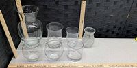 Seven clear glass vases lined up with rulers for scale