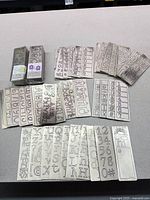 Full lot showing packaged sets and numerous loose metal stencil plates laid out on table