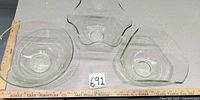 Top view of three clear pale-green glass bowls with scalloped rims beside ruler