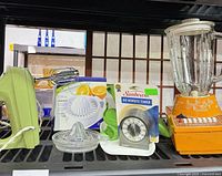All five items displayed on shelf: hand mixer, boxed citrus juicer, Sunbeam timer, glass juicer, orange blender with jar