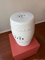 Front view of white ceramic garden stool showing pierced motifs and studded banding
