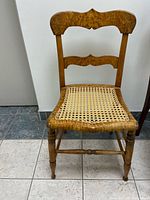 Front view of tiger maple slat-back side chair showing carved crest, woven cane seat and turned legs