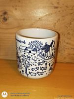 Front view of white ceramic shot cup with blue Danish village illustration and 'Denmark' text