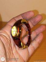 Watch held in hand showing faux amber resin bracelet and oval dial