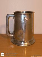 Full view of pewter tankard front with handle and pennant emblem