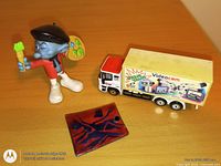 Smurf figurine, toy truck, copper enamel pendant on wooden surface