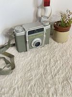 Front angled view showing lens, name plate, green body panels, attached strap