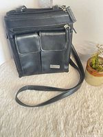 Front view of black faux leather organizer bag showing two patch pockets, strap and plaque