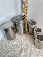 group of five graduated stainless steel canisters with measuring tape for scale