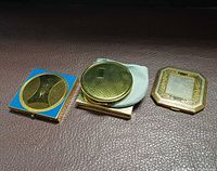 Front view of three gold-tone compacts: square blue enamel, round, octagonal