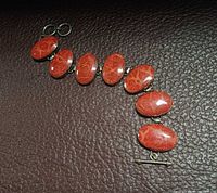 Bracelet laid flat showing seven red jasper cabochons and toggle clasp
