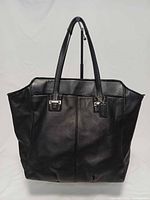 Front view of black leather Coach Taylor tote showing shape, handles and hangtag