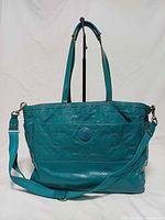 front view showing embossed pattern, logo patch, handles and shoulder strap