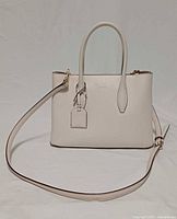 Front view of beige leather Kate Spade Eva small satchel with crossbody strap attached and hanging tag