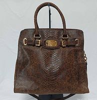 Front view of brown snakeskin-embossed leather satchel showing handles, front strap with gold MK plate