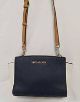 Front view showing navy body, white side panels, gold logo, adjustable tan strap