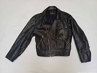 Full front view of black leather motorcycle jacket laid flat showing overall design