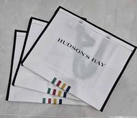 Three flat-packed Hudson's Bay tote bags stacked, showing logo, stripes and black trim