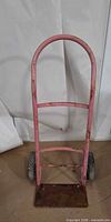 Front view showing entire pink metal hand truck with toe plate and wheels