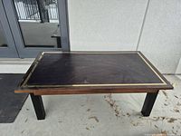 Full view of rectangular coffee table, dark top with brass border, black legs