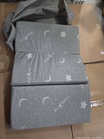 Folded grey tri-fold mattress with moon/star print partially inserted into grey carrying case